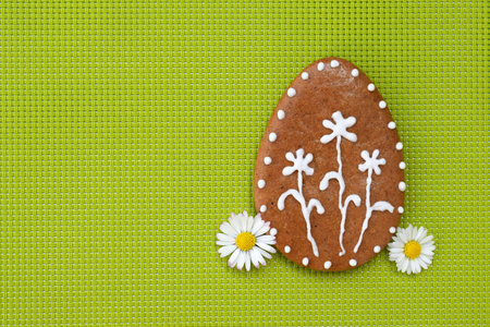 Decorated Easter gingerbread cookie in a shape of egg, with daisy flowers, green background, copy space for textの写真素材