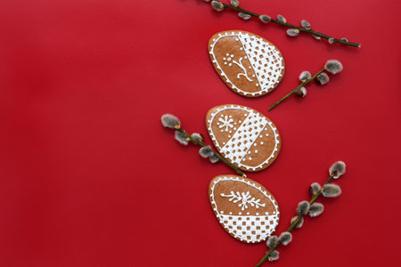 Romantic decorated Easter gingerbread cookies in a shape of egg, with willow twigs, red background, copy space for textの写真素材