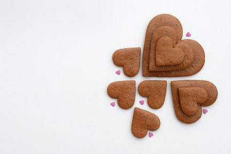 Undecorated heart-shaped gingerbread cookies in three sizes with small sugar hearts on a white background, copy space for textの写真素材