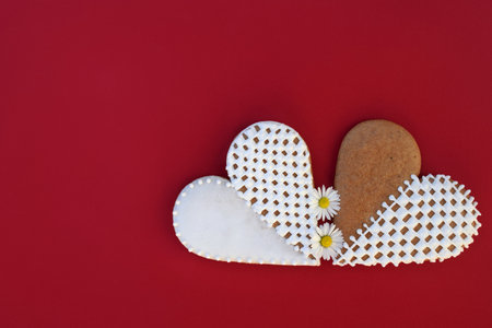 Gingerbread hearts decorated with white icing, with daisy flowers, red background, copy space for textの写真素材