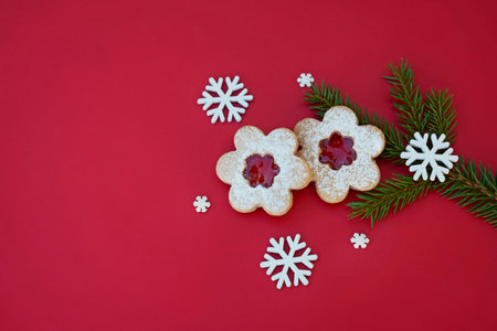 Linzer cookies in a shape of flower on a red background with spruce twig and snowflakes, copy space for textの写真素材
