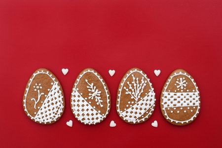 Decorated Easter gingerbread cookies in a shape of egg, with small sugar hearts, red background, copy space for textの写真素材