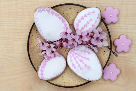 Plate with Easter gingerbread cookies in a shape of egg and flower, decorated with white and pink...