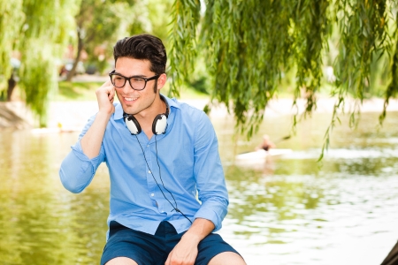 handsome man wearing glasses talking on the phone and smiling by the river の写真素材