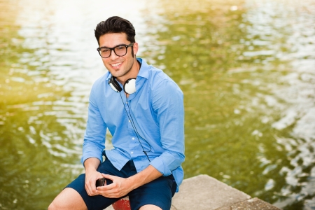 handsome man wearing glasses talking on the phone and smiling by the river の写真素材