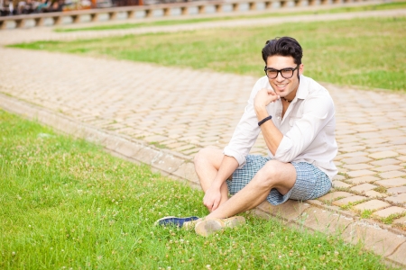 handsome man sitting on the sidewalk and smiling at the cameraの写真素材