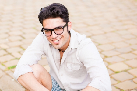 handsome man wearing glasses sitting on the sidewalk and smiling at the cameraの写真素材