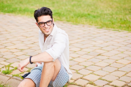 handsome man wearing glasses sitting on the sidewalk smilingの写真素材
