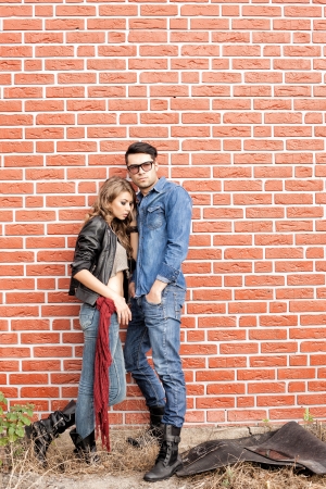 attractive fashionable couple casually leaning against brick wall の写真素材