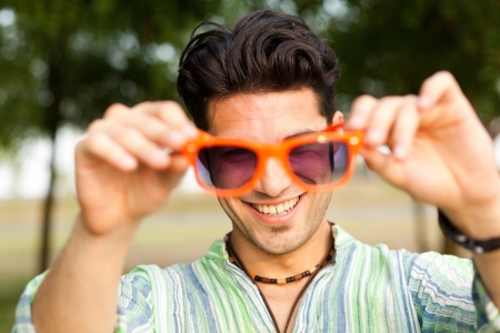 handsome man holding a pair of orange sunglasses and smilingの写真素材