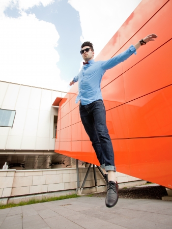 attractive young male model jumping outdoors in blue shirt and sunglassesの写真素材