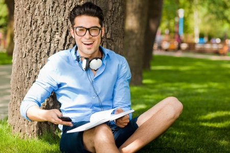 smiling man holding a book on the grass in the parkの写真素材