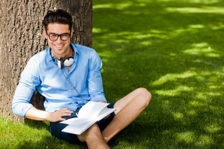 smiling man holding a book on the grass in the parkの写真素材