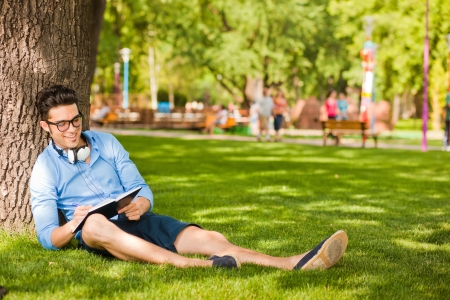 handsome man writing something and relaxing on the grass in the parkの写真素材