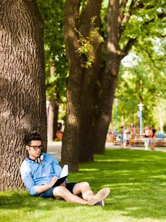 handsome man writing something and relaxing on the grass in the parkの写真素材