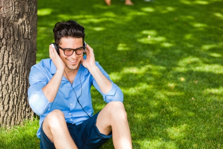 handsome man smiling and listening to music on the grass in the parkの写真素材