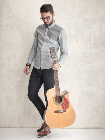 handsome man holding an acoustic guitar against grunge wallの写真素材