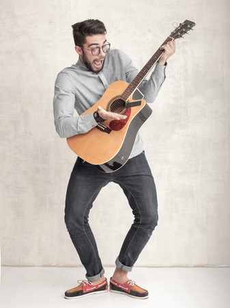 handsome funny man playing an acoustic guitar against grunge wallの写真素材