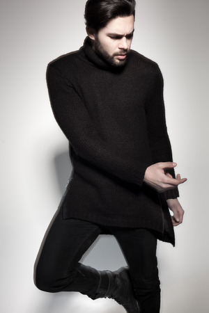 sexy fashion man model in black sweater, jeans and boots posing dramaticの写真素材