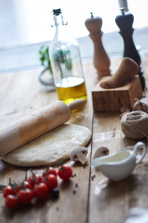 Cherry tomatoes, dough, rolling-pin, olive oil, mortar and pestle lying on table. Other ingredients for pizzaの写真素材