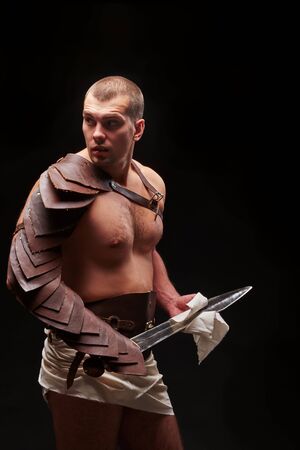 male gladiator with sword and armor on a black background looks into the camera. studio shotの写真素材