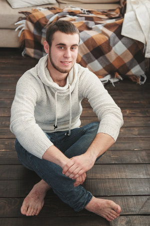 Handsome man wearing a white jacket and jeans sitting down intsideの写真素材