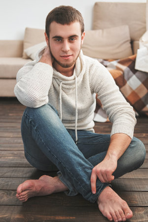 Handsome man wearing a white jacket and jeans sitting down intsideの写真素材