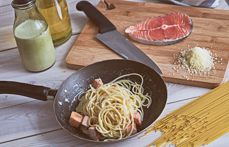 Close up of pasta with red fish and cheese in a frying pan on a white wooden tableの写真素材
