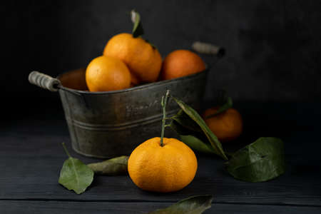 Several tangerines with leaves in a container lie on a black table against a dark background. Rustic style copyspace.の写真素材