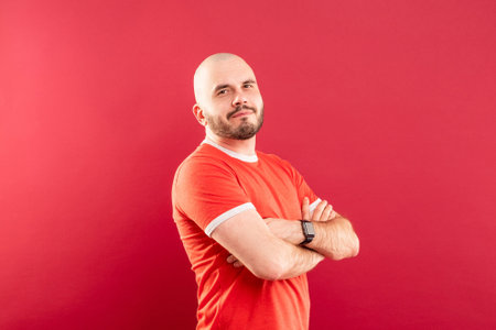 A middle-aged man with a beard in a red T-shirt on a red background joyfully points to the right. Isolated.の写真素材