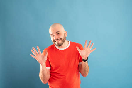 A bald middle-aged man with a beard and in a red T-shirt on a blue background. Shows his palms towards the viewer. Shows that his hands are empty.の写真素材