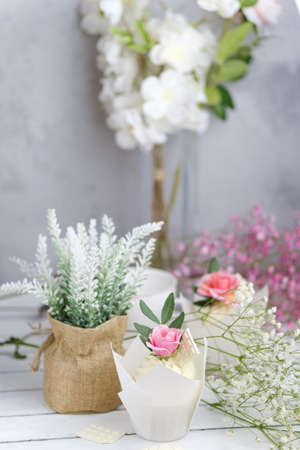 Several cupcakes and muffins with white butter cream and a lively pink rose on a white wooden table. Valentines day or Mothers Day gift. Rustic style.の写真素材