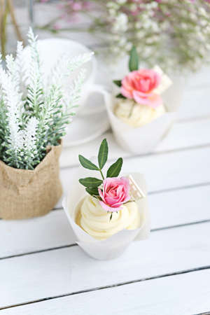 Several cupcakes and muffins with white butter cream and a lively pink rose on a white wooden table. Valentines day or Mothers Day gift. Rustic style.の写真素材