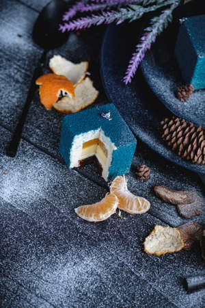 Blue cake filled with orange and tangerine in the shape of a cube. Nearby on a black table are ingredients oranges, tangerines, nuts. Rustic styleの写真素材