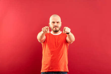 A middle-aged man with a beard in a red T-shirt on a red background stands rejoicing in victory. Isolated.の写真素材