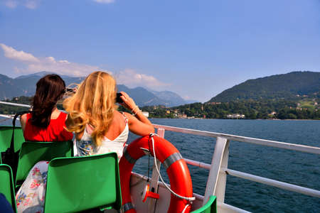 young women take pictures with cell phones from the boat on lake como italyのeditorial素材