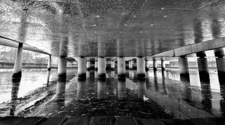 Concrete pillars underneath a bridge reflecting in the water abstract impression in black and whiteの写真素材