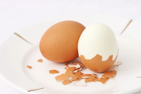 A cooked egg peeled and standing with eggshell pieces.