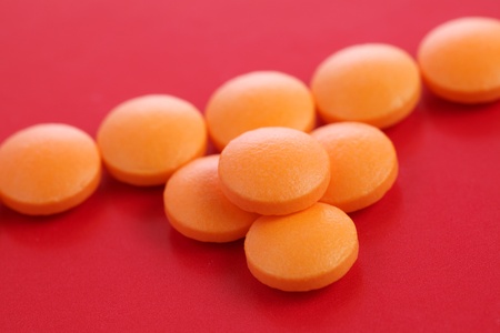 Many orange pills put together on red background.