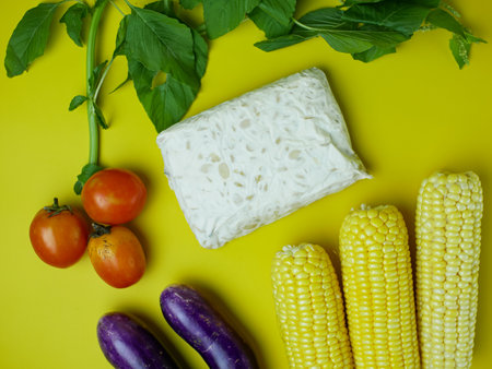 the concept of healthy food consists of eggplant, spinach, tomatoes, and corn. vegetarian food. isolated on a yellow backgroundの写真素材