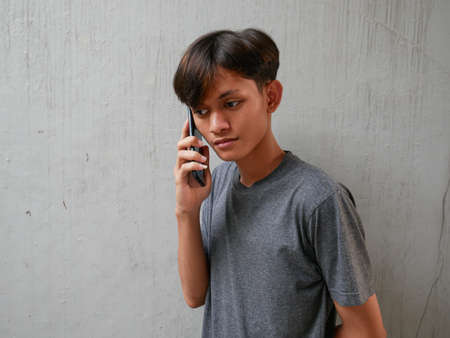 young asian man is on the phone with a sad and disappointed expressionの写真素材
