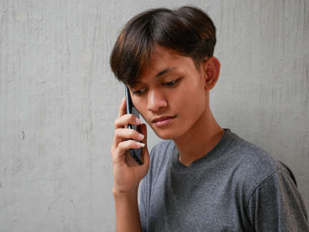 young asian man is on the phone with a sad and disappointed expressionの写真素材