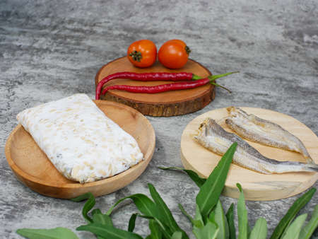 salted fish, raw tempeh and vegetables on a wooden cutting board. kitchen food conceptの写真素材