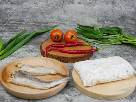 salted fish, raw tempeh and vegetables on a wooden cutting board. kitchen food conceptの写真素材