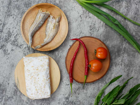 salted fish, raw tempeh and vegetables on a wooden cutting board. kitchen food concept
