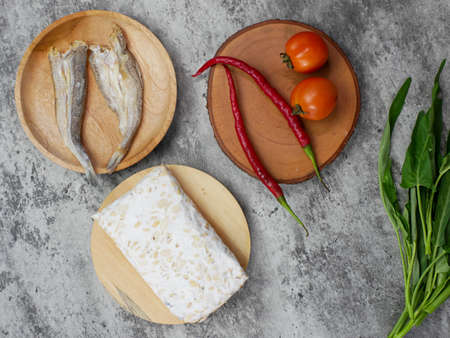 salted fish, raw tempeh and vegetables on a wooden cutting board. kitchen food conceptの写真素材