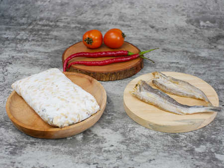 salted fish, raw tempeh and vegetables on a wooden cutting board. kitchen food conceptの写真素材