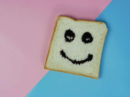 white bread with smiley emoticon on blue and pink pastel backgroundの写真素材