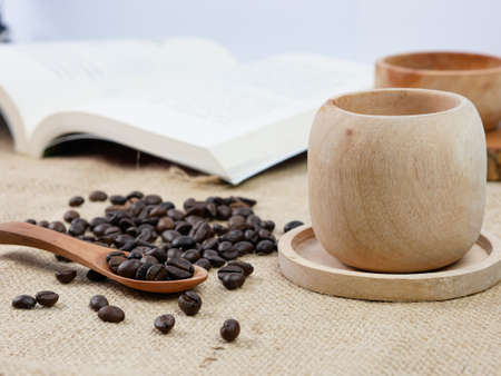 Wooden cup of coffee with coffee beans and book with blur background. morning activitiesの写真素材