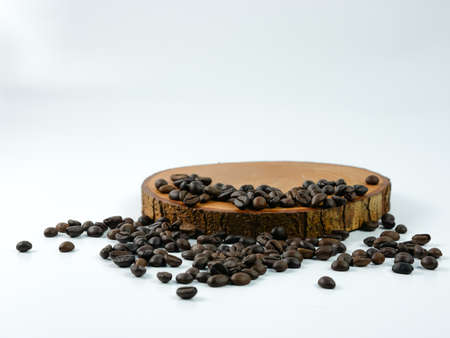 Coffee beans scattered on a round wooden plank isolated on a white background. Product placement concept.の写真素材